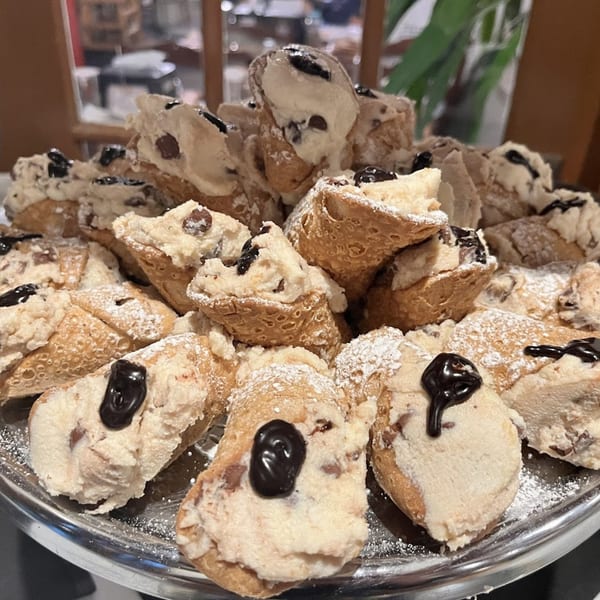 A silver platter piled high with cannolis, dusted with powdered sugar and drizzled with chocolate.