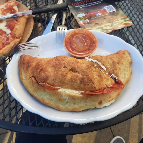 A golden-brown pepperoni calzone with melted cheese and a side of marinara sauce on a white plate.