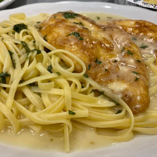 Chicken Alfredo with linguine pasta and parsley in a creamy white sauce on a white plate.