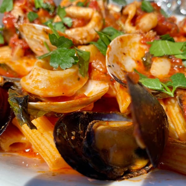 Close-up of pasta with mussels, clams, and calamari in red sauce, garnished with parsley.