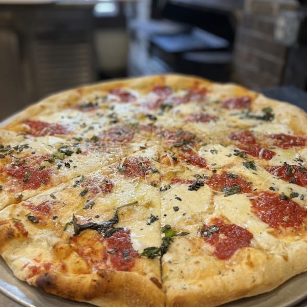 A freshly baked Bear Mountain Pizza, sliced, with melted cheese, red sauce, and herbs.
