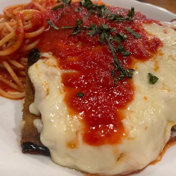Eggplant parmesan with melted mozzarella, red sauce, basil, and a side of spaghetti.
